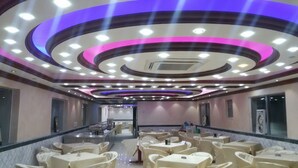 Une salle de conférence d’hôtel avec des tables rondes, une scène et un design moderne au plafond.