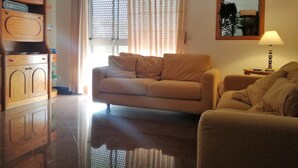 Ein Wohnzimmer mit einer Couch, einem Holzschrank, einer Lampe und einem Fenster mit Vorhängen.