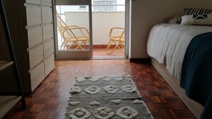Ein Schlafzimmer mit einem Bett, einem Holzschrank, einem gemusterten Teppich und einem Balkon mit zwei Korbstühlen.