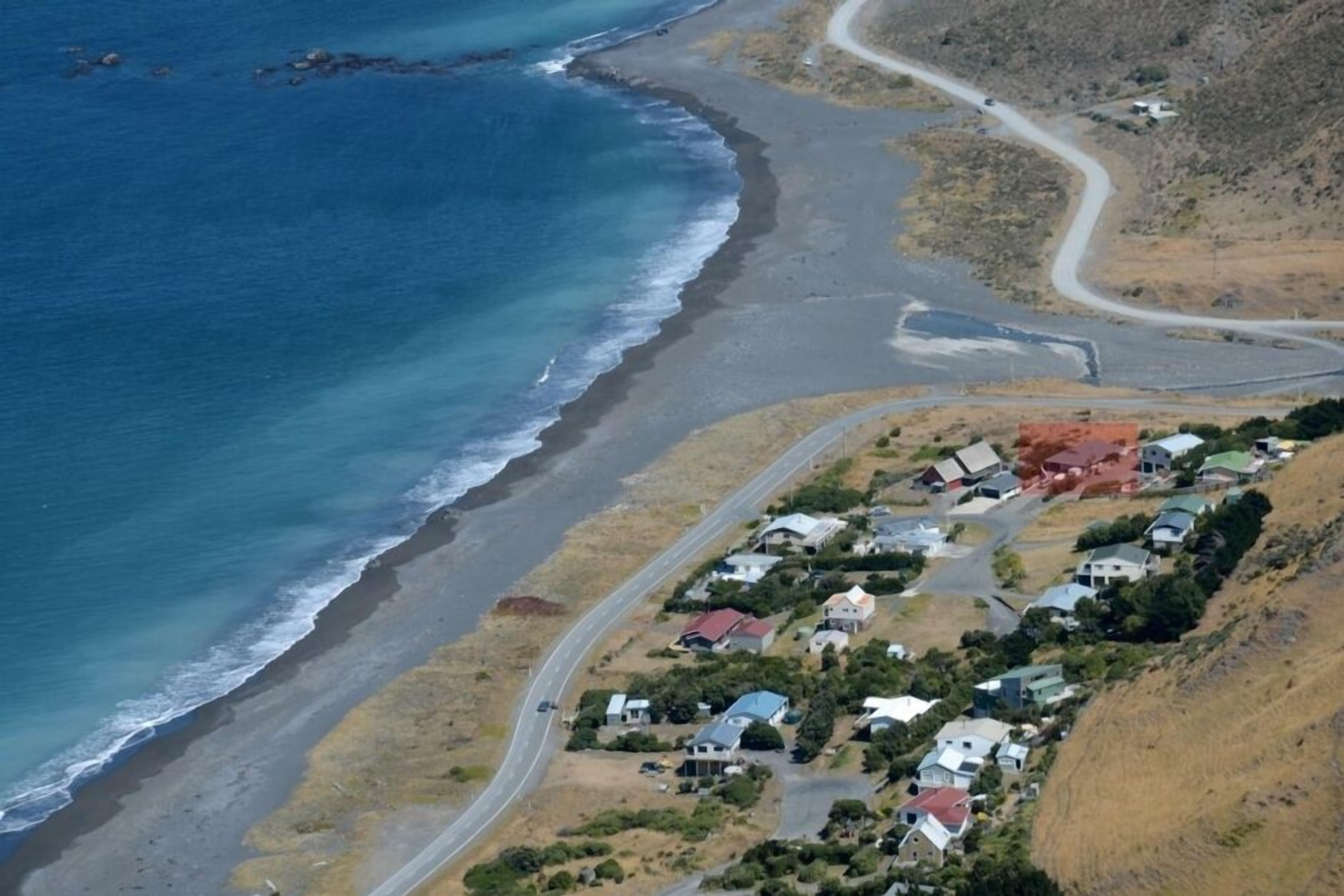 An aerial view of a coastal area with houses along a curved road, a beach, and a road leading to a settlement.