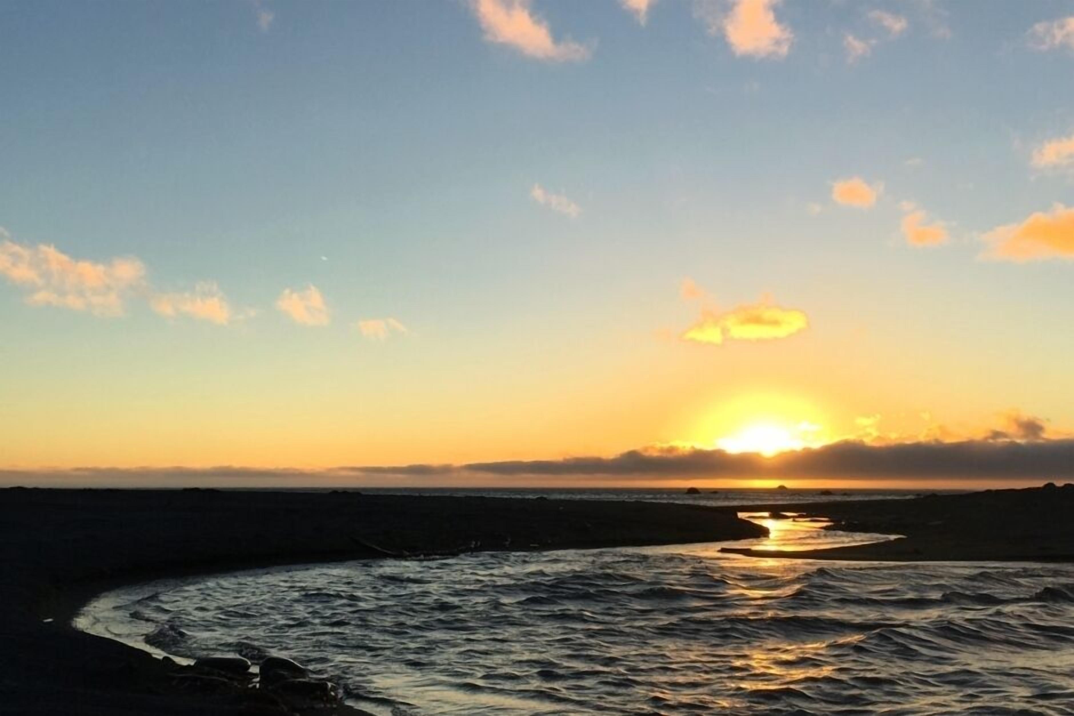 A sunset over a coastal landscape with a river curving through the scene.