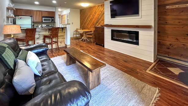 A modern living room with a leather sofa, wooden coffee table, and a TV mounted on a wooden wall. - Ski-in/Ski-out, 1 bedroom at the heart of the Resort Base Area! (Mt. Crested Butte)