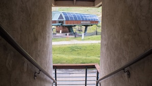 A view from a covered area to a building labeled "SILVER QUEEN" with a solar panel roof, a staircase, and a grassy area in the background. - Ski-in/Ski-out, 1 bedroom at the heart of the Resort Base Area! (Mt. Crested Butte)