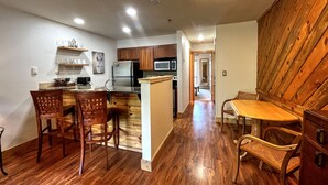 A compact kitchen with wooden cabinets, a central island, and a dining area with a wooden table and chairs. - Ski-in/Ski-out, 1 bedroom at the heart of the Resort Base Area! (Mt. Crested Butte)