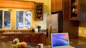 A kitchen with wooden cabinets, a stainless steel refrigerator, a laptop on the counter, and a window with a view of trees. - Large group(walking distance to Alyeska Resort) (girdwood)