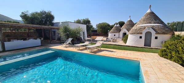 A swimming pool with lounge chairs, a stone building, and a white structure with conical roofs. - Trulli Sant'Oronzo: private pool, olive trees and sandy beaches at your doorstep (Monopoli)