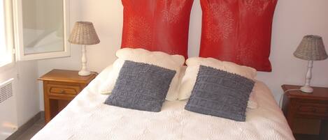 A neatly made bed with a white and grey quilt, two red curtains, and two bedside lamps on wooden nightstands.