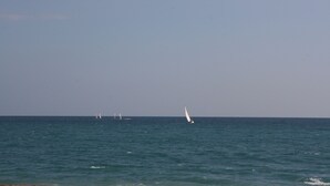 Blick auf das Meer mit einem Segelboot und einigen weiteren Booten in der Ferne.