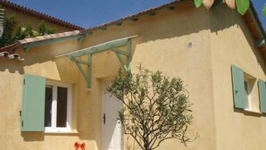 Ein Gebäude mit gelber Fassade, grünen Fensterläden und einem kleinen Baum davor.