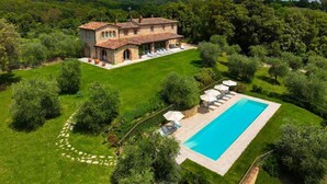 Une grande maison en pierre dotée d’une piscine, entourée d’une végétation luxuriante et d’une pelouse bien entretenue.