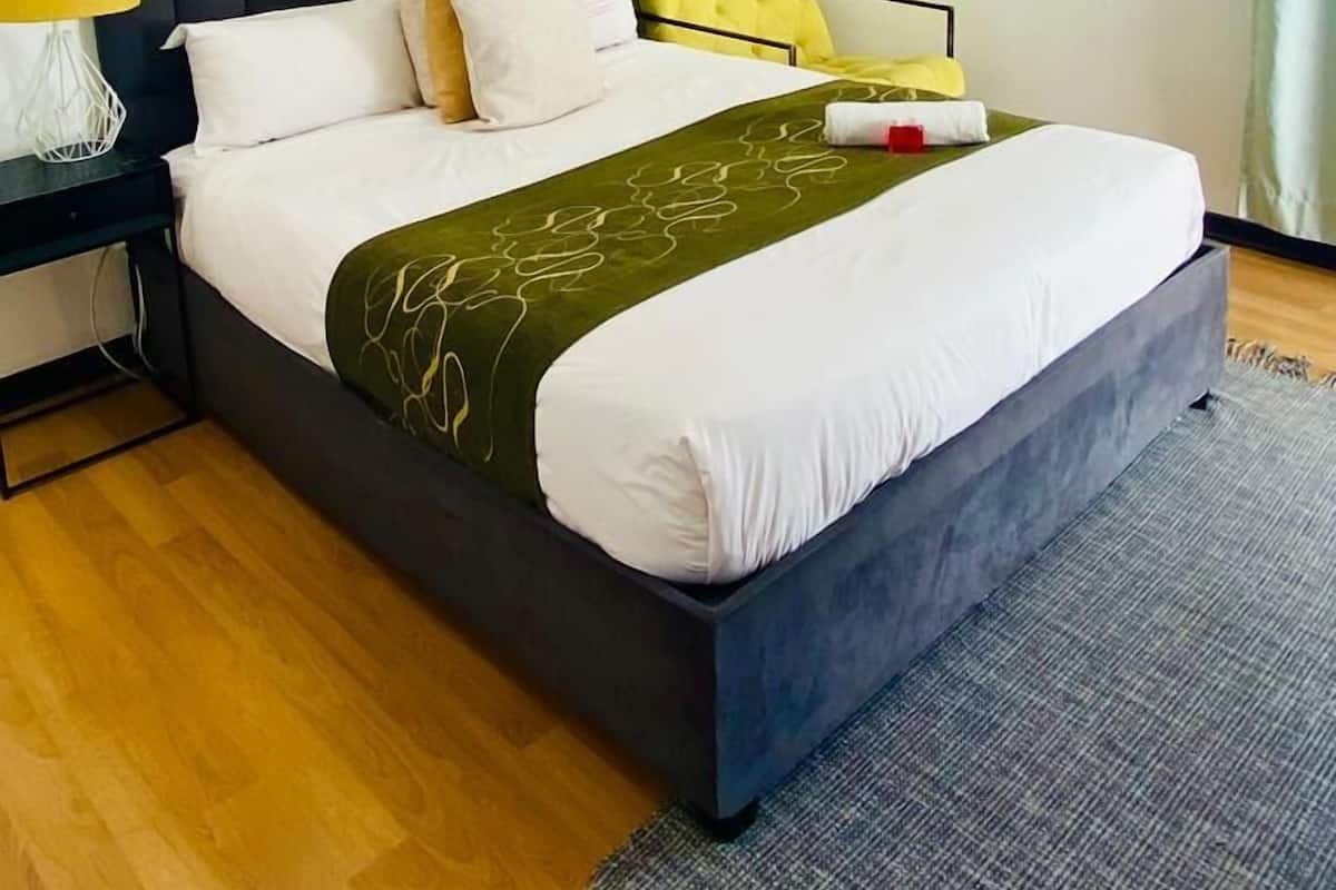 Une chambre d’hôtel bien rangée, avec un grand lit, une table de chevet avec une lampe et deux tableaux encadrés au mur.