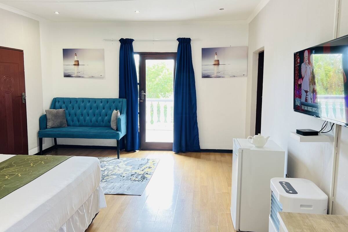 Une chambre d’hôtel avec un lit, un canapé bleu, une télévision et un petit réfrigérateur blanc.