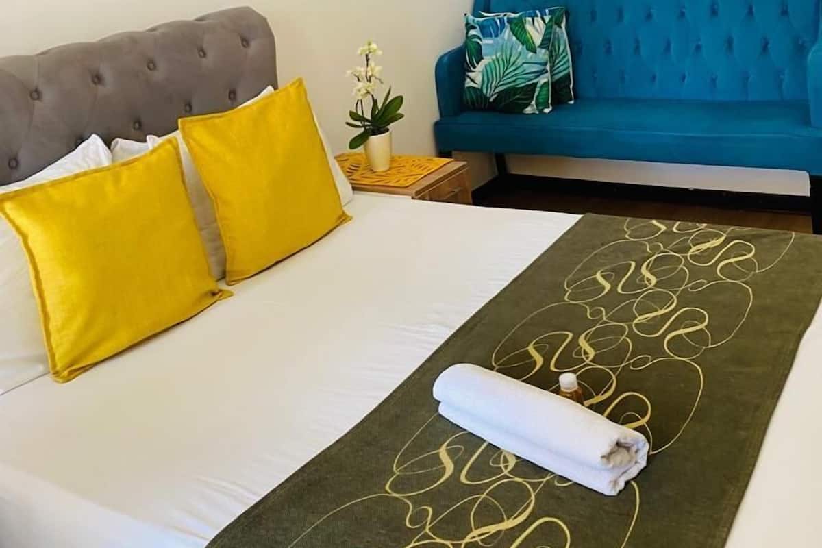 Un lit bien fait, avec une couverture verte, une tête de lit grise à motifs et deux oreillers jaunes.
