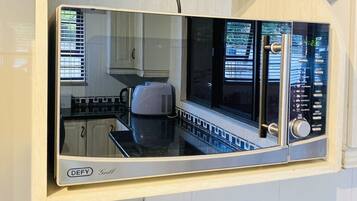Una cocina con microondas integrado, cafetera y un reloj digital en la pared.