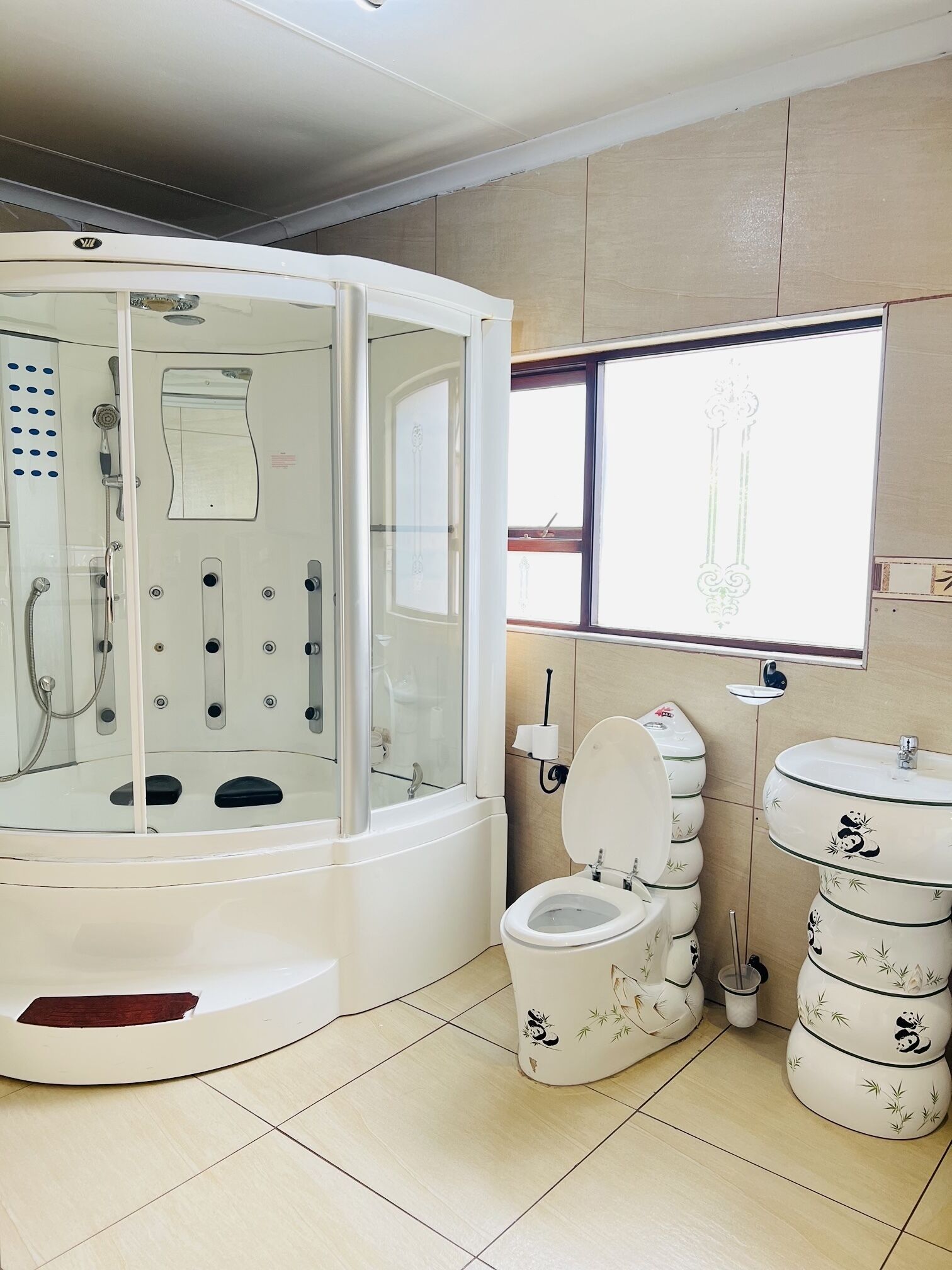 Moderni kylpyhuone, jossa on lasiseinällä varustettu suihku, pandakuviollinen wc-istuin ja samantyylinen pesuallas.