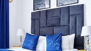 A modern bedroom with a dark headboard, white bedding, and blue accent pillows. - Airport Royal Guest House (Kempton Park)