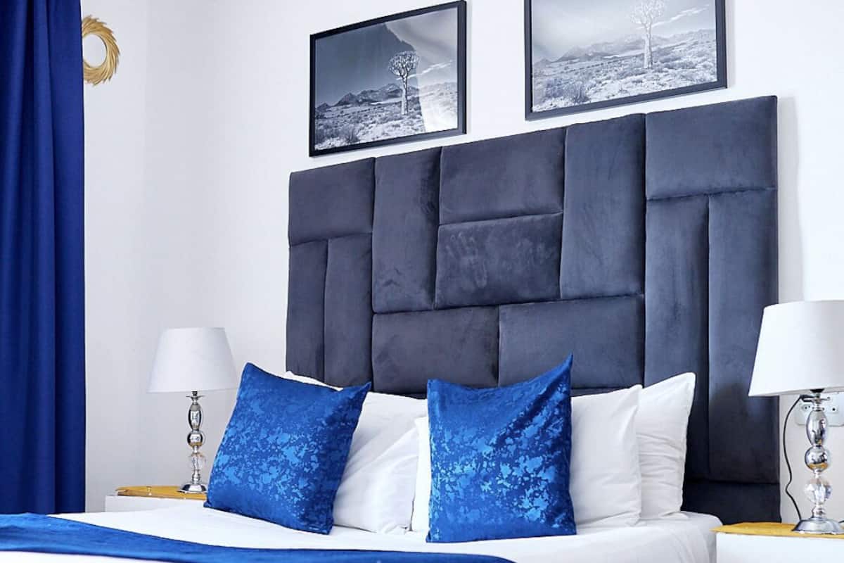 Une chambre moderne avec une tête de lit sombre, une literie blanche et des coussins d’accent bleus.