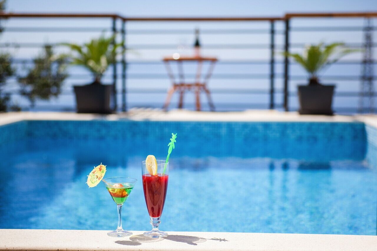 A poolside area with two cocktails on a table, a lifeguard chair, and potted plants in the background.