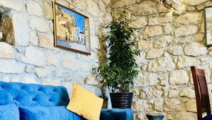 Ein Zimmer mit einer Steinwand, einem blauen Sofa, einem gelben Kissen, einer Topfpflanze und einem kleinen Tisch mit einer Fernbedienung.