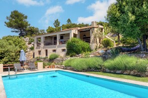 A pool with lounge chairs and umbrellas, a stone building with balconies, and surrounding greenery. - 9 Guest Villa with Heated Pool, Spa, Pétanque & Panoramic View (Tourtour)