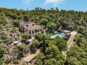 A modern house with a swimming pool, surrounded by dense forest and rocky terrain. - 9 Guest Villa with Heated Pool, Spa, Pétanque & Panoramic View (Tourtour)