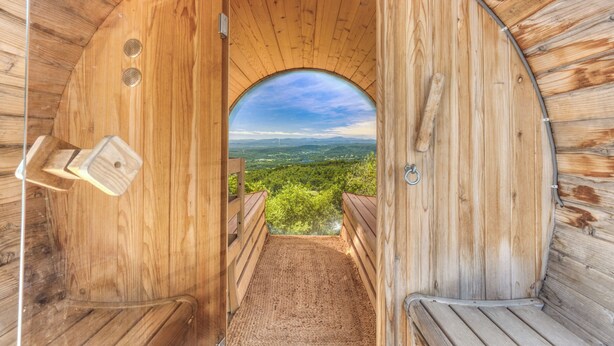 Uma sauna de madeira com vista para uma paisagem verde através de uma abertura em arco.