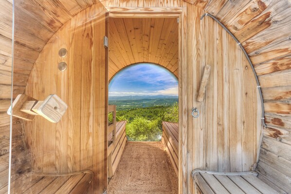 Un sauna en bois offrant une vue sur un paysage verdoyant, visible à travers une ouverture en arc de cercle.