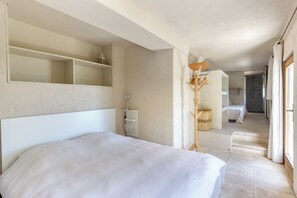 A bedroom with a bed, a shelf, a bedside table, a lamp, a wardrobe, and a bathroom in the background. - 9 Guest Villa with Heated Pool, Spa, Pétanque & Panoramic View (Tourtour)