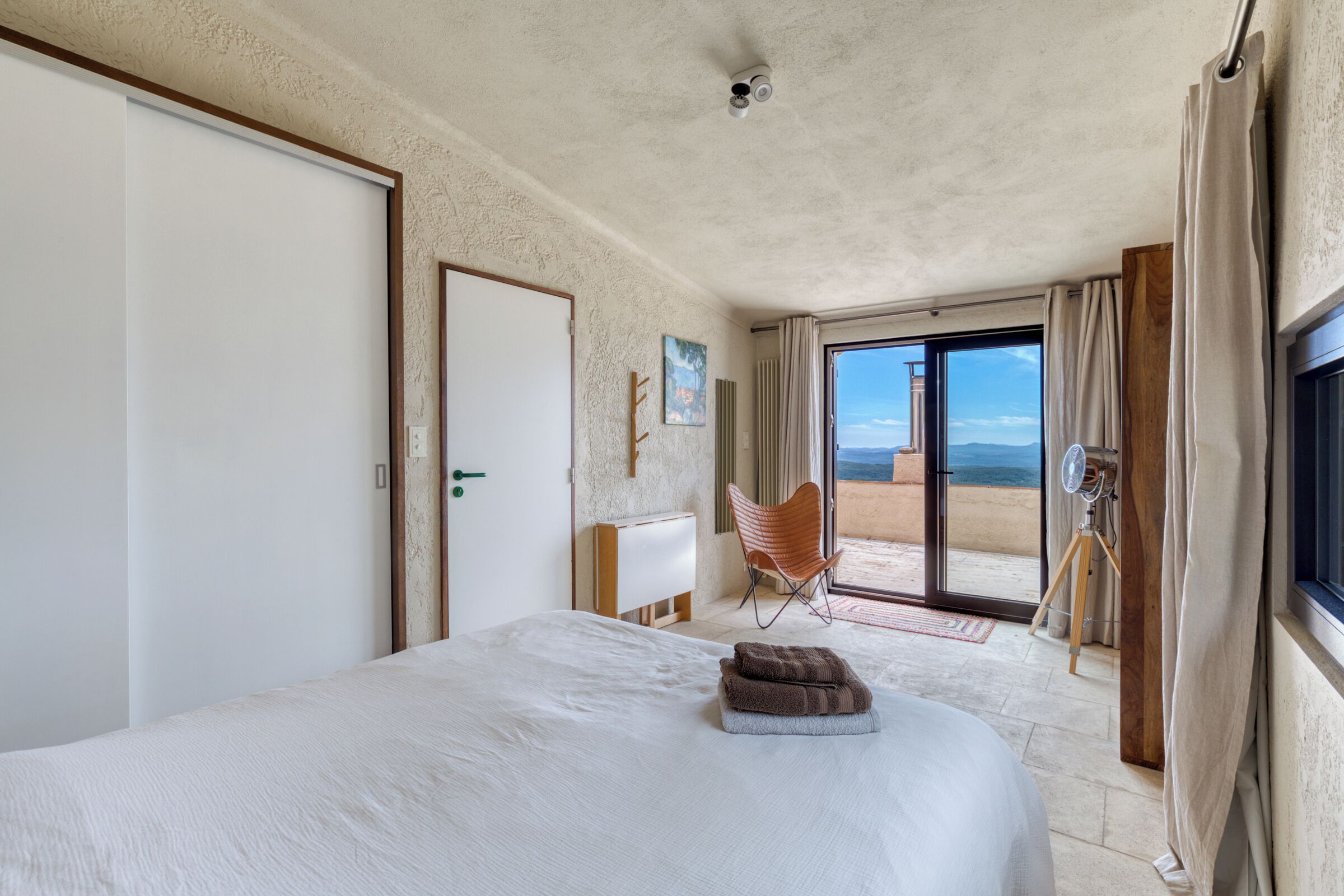 Une chambre avec un grand lit, une chaise, un bureau et une vue sur l’extérieur.
