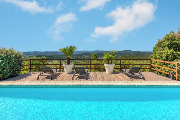 A pool with lounge chairs and potted plants on a wooden deck with a view of hills. - 9 Guest Villa with Heated Pool, Spa, Pétanque & Panoramic View (Tourtour)
