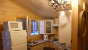 Una cocina compacta con armarios de madera, microondas, refrigerador y una mesa de comedor.