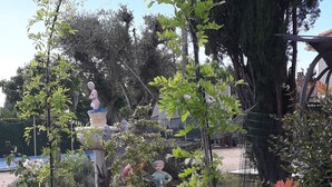 Un jardín con estatuas, una fuente y diversas plantas.