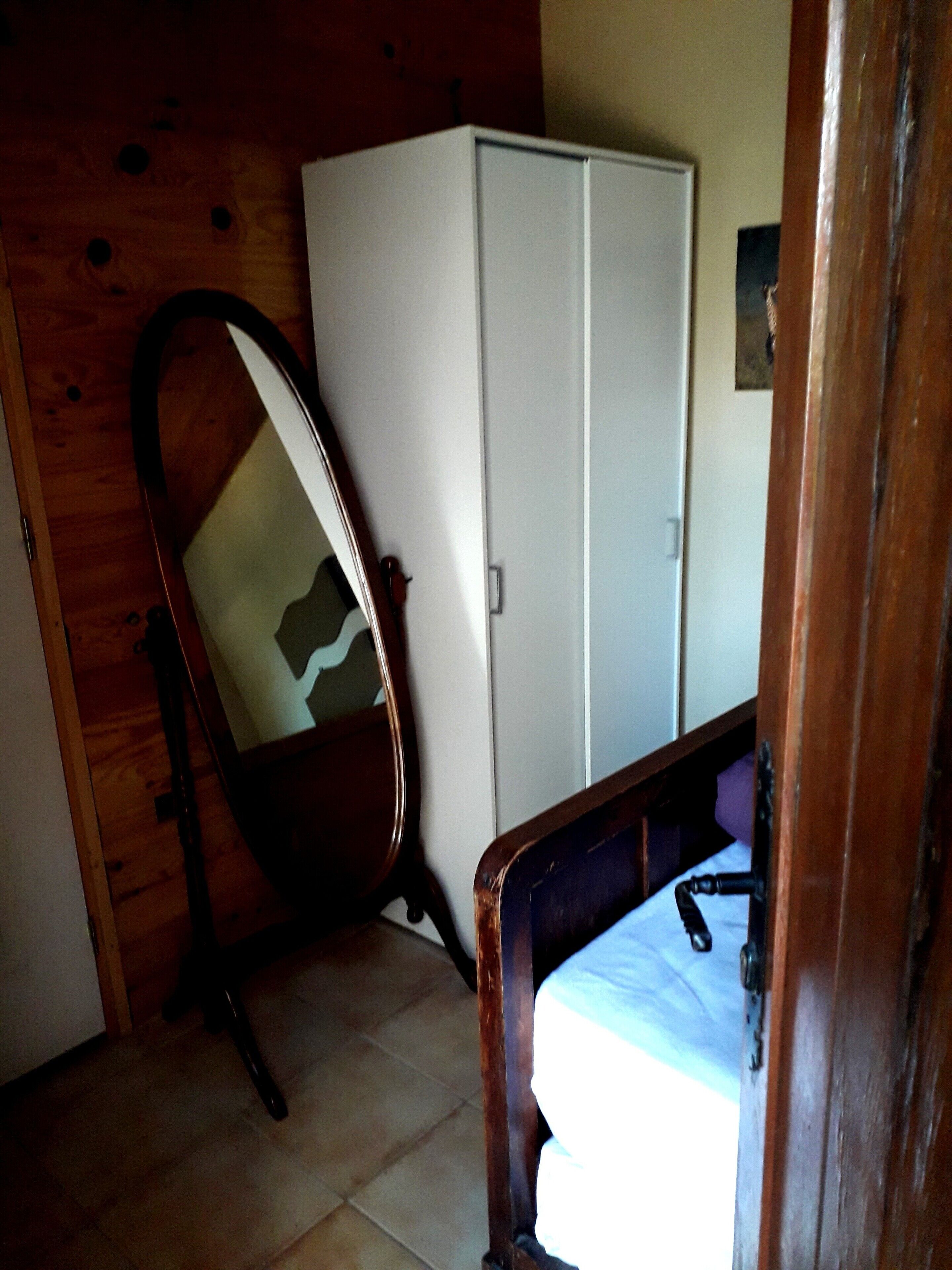 Une pièce avec un plancher en bois, une armoire blanche et une chaise en bois.