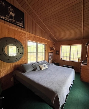 A wooden-paneled room with a bed, a round mirror, and a window with a view.