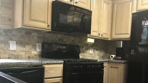 Una cocina con encimeras de granito, un microondas negro, una estufa y armarios de madera.