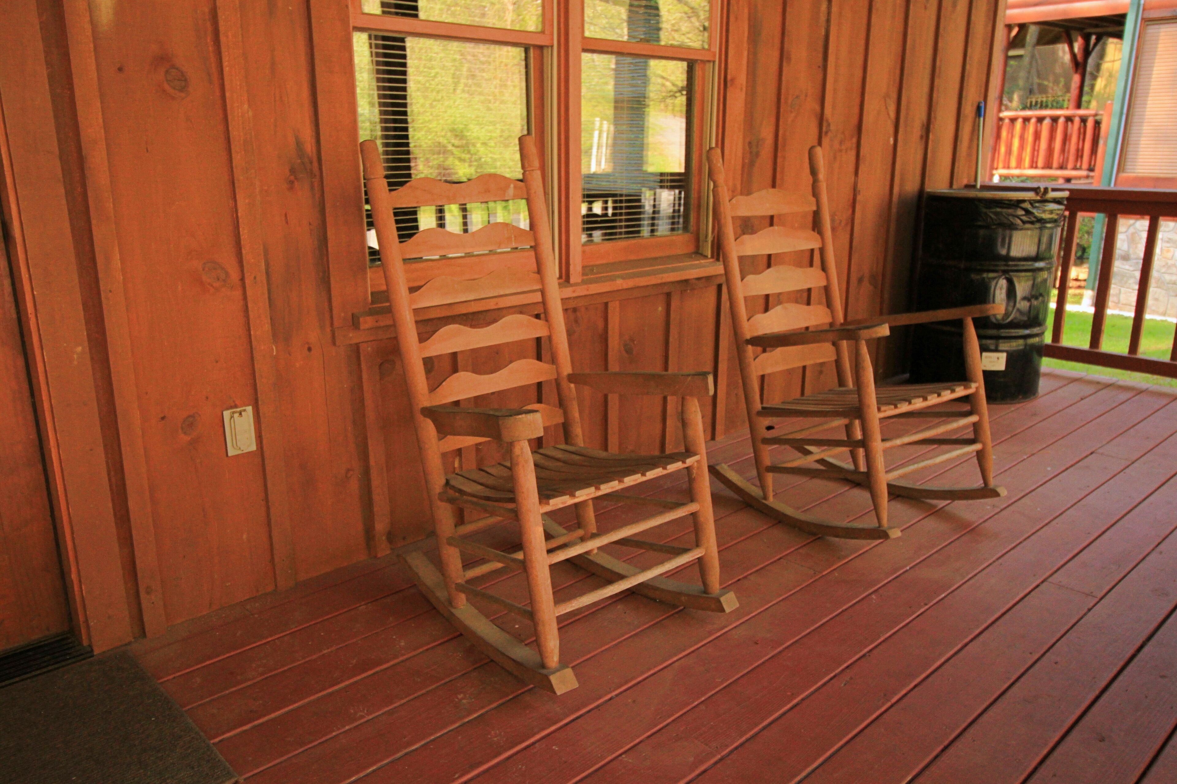 Two wooden rocking chairs on a wooden porch with a window and a barrel.