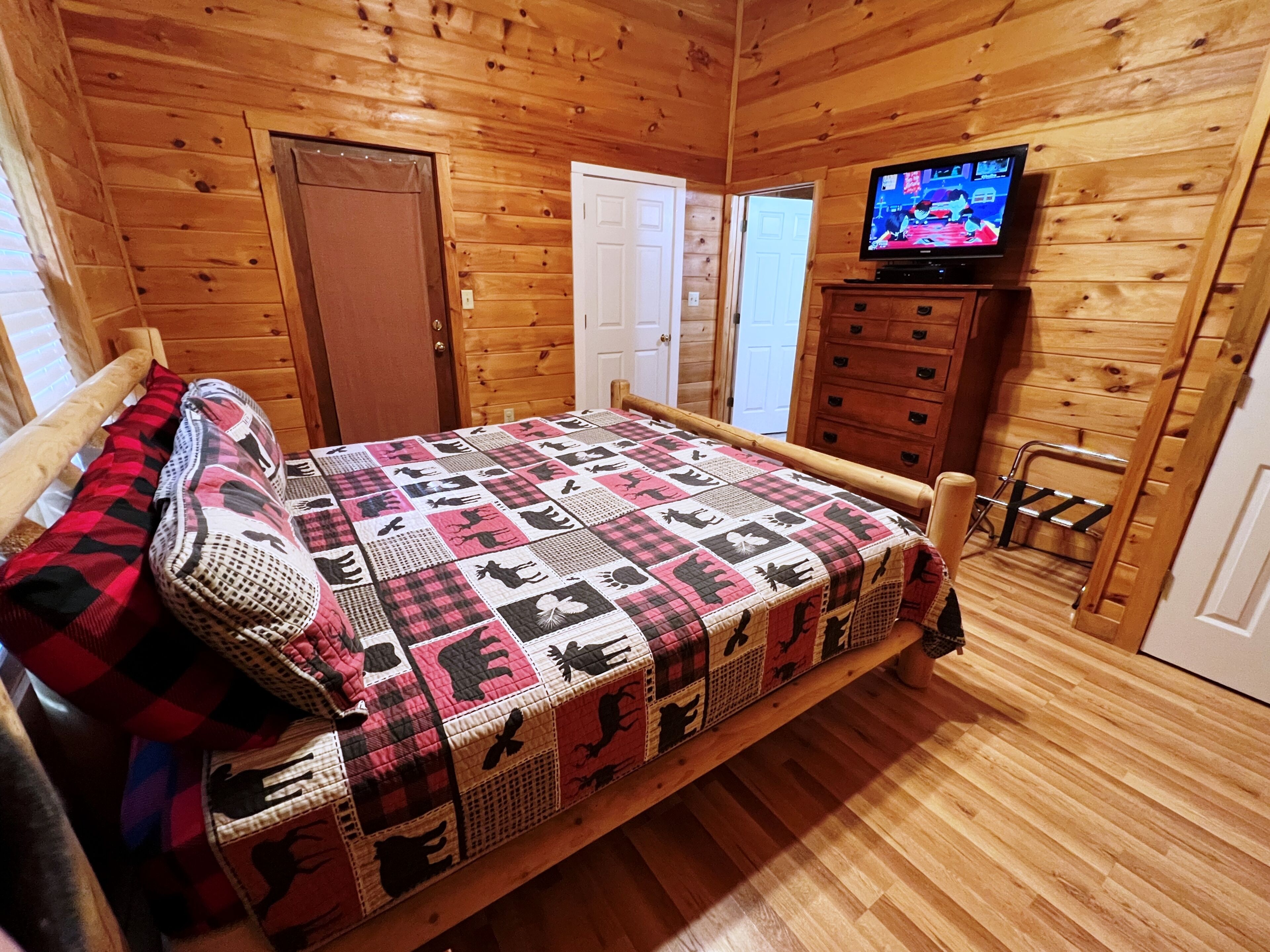A wooden cabin room with a bed, a television, and a dresser.