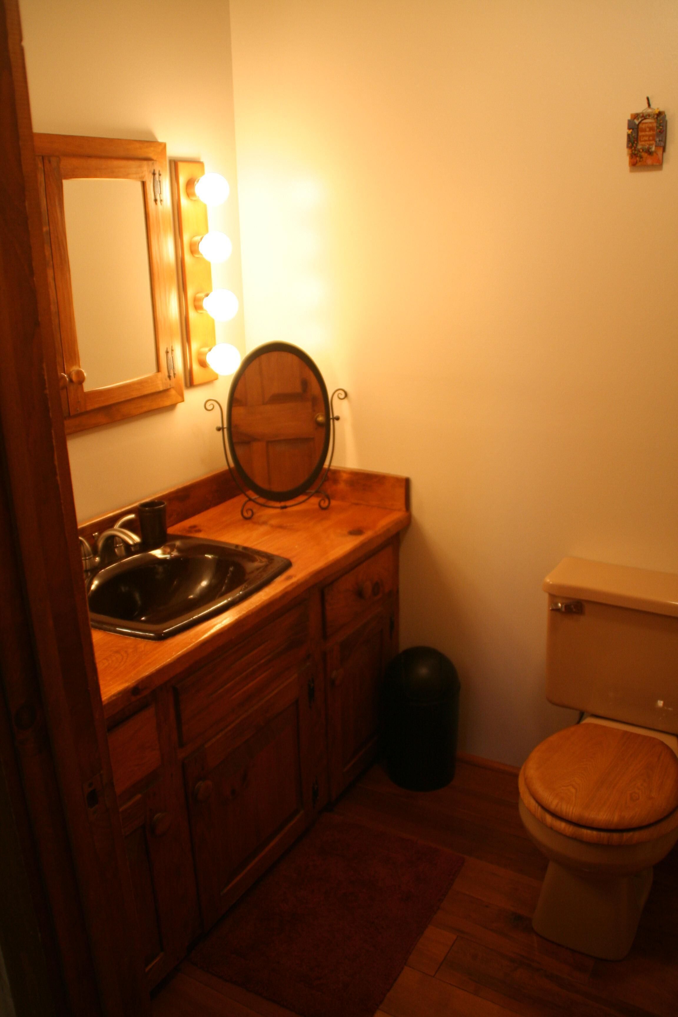 Un baño con tocador de madera, un lavabo, un espejo con luces, un inodoro y un cubo de basura.