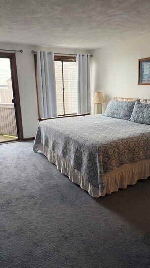 A bedroom with a large bed, a window with curtains, a lamp, and a view of a brick wall outside.
