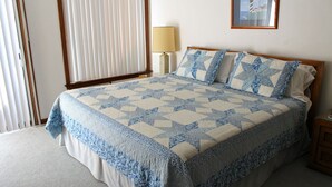 Ein Schlafzimmer mit Bett, Nachttisch, Lampe, Fenster mit Jalousien und einem gerahmten Bild an der Wand.