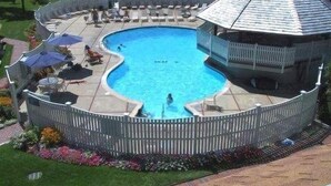 Ein runder Swimmingpool mit Holzterrasse und einem pavillonartigen Gebäude.