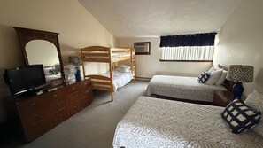 A bedroom with bunk beds, a dresser, a television, and a window with blinds.
