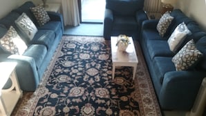Ein Wohnzimmer mit einem dunkelblauen Sofagarnitur, einem weißen Couchtisch und einem gemusterten Teppich.