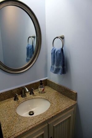 A bathroom with a granite countertop sink, a round mirror with a decorative frame, and two blue towels hanging on a towel rack.