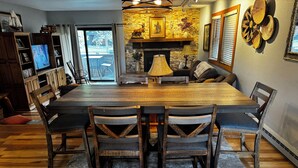 Un comedor con una gran mesa de madera, sillas de madera oscura, una chimenea y un televisor al fondo.