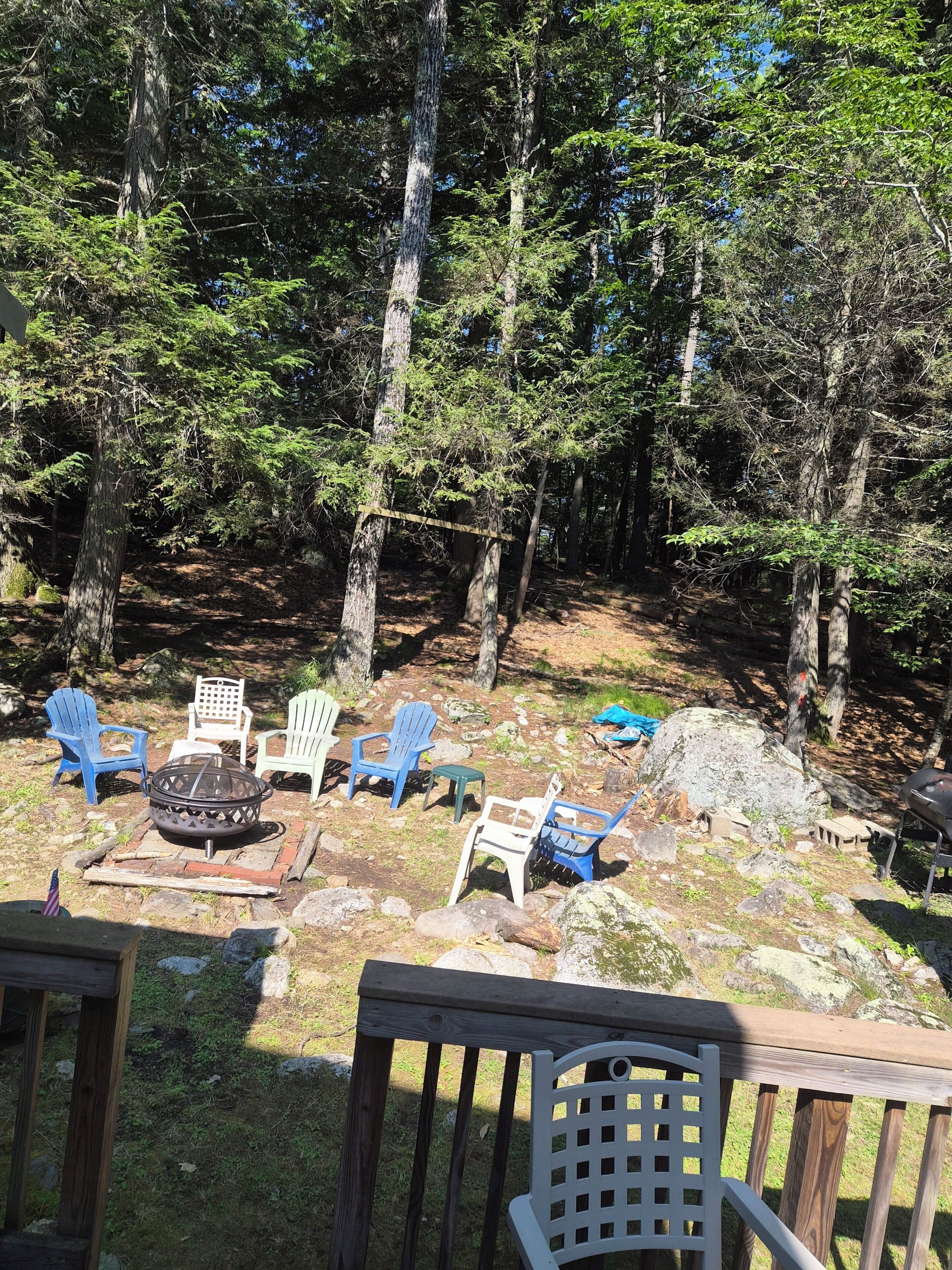 Une terrasse avec coin salon extérieur, un foyer et un espace barbecue, le tout entouré d’arbres.