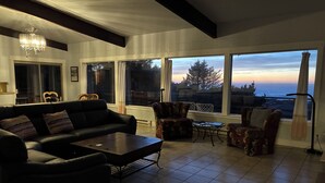 Un soggiorno con un divano nero, cuscini decorati, un tavolino da caffè e vista sull'oceano al tramonto.