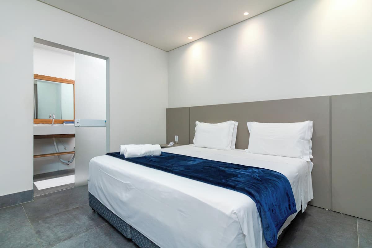 A modern hotel room with a large bed, a built-in wardrobe, and a bathroom with a mirror and sink.