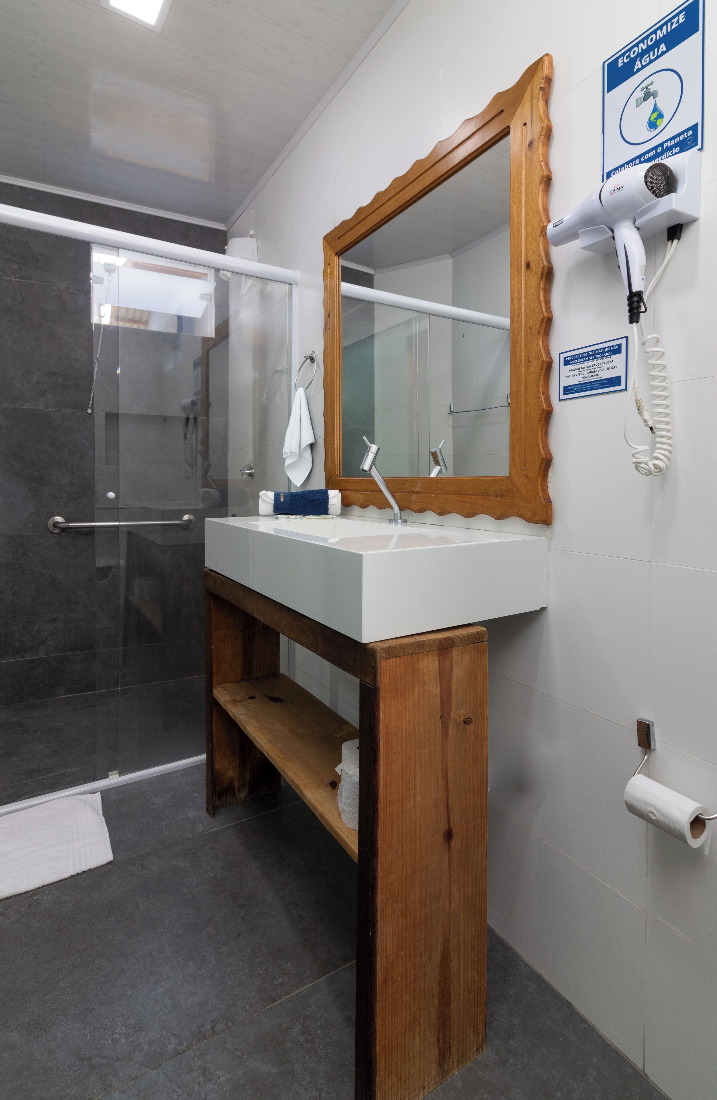 A bathroom with a wooden vanity, a mirror, a towel rack, a hairdryer, and a toilet paper holder.