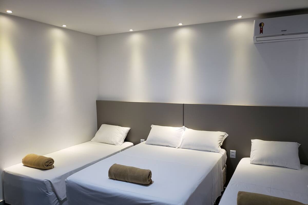 A hotel room with three single beds, each with a white mattress and a beige towel.
